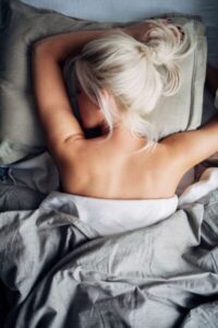 Eine Frau, die auf dem Bauch in grauen Bettdecken schläft. Bild zum Thema Zeitumstellung