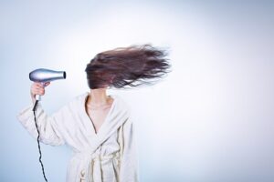 Eine Frau im weißen Bademantel föhnt sich die Haare über das Gesicht. Bild zum Thema: Beauty-Tipps für die Haare