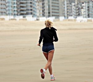 Die sportliche Frau rennt am Strand in Shorts und einem Pullover. Bild zum Thema: Mommy makeover, Fit durch die Schwangerschaft – um jeden Preis?