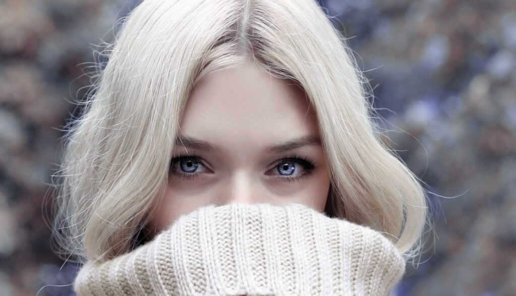 Eine Blondine und blauen Augen versteckt sich bis zur Nase in ihrem Pullover. Bild zum Thema: Byebye Doppelkinn - Belkyra behandlung